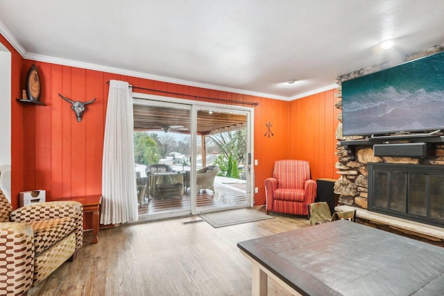 living area featuring wood-type flooring, a stone fireplace, and crown molding