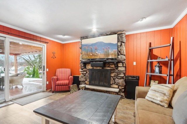 living room featuring a stone fireplace, ornamental molding, wooden walls, and light hardwood / wood-style flooring