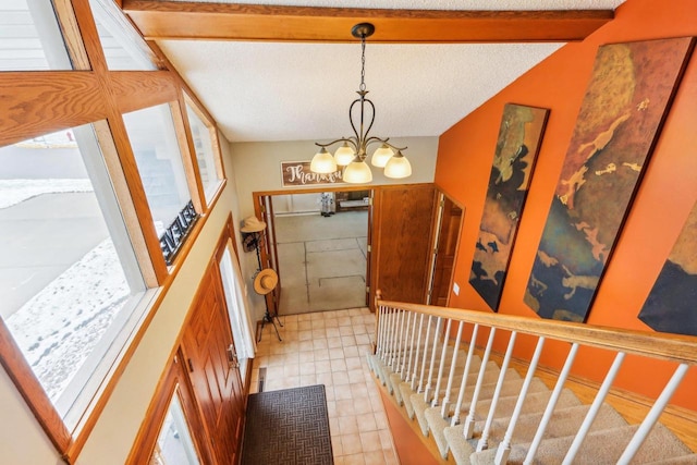 entryway featuring a chandelier, a textured ceiling, and vaulted ceiling with beams