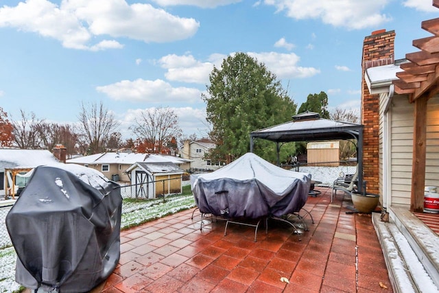 snow covered patio with a gazebo, grilling area, and a storage shed