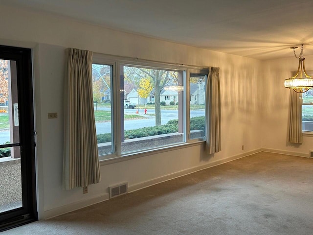 unfurnished room featuring a chandelier, carpet floors, and a healthy amount of sunlight