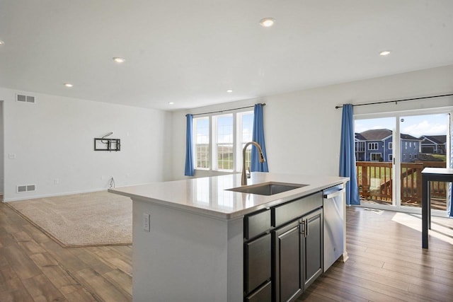 kitchen featuring dark wood-type flooring, sink, dishwasher, and an island with sink