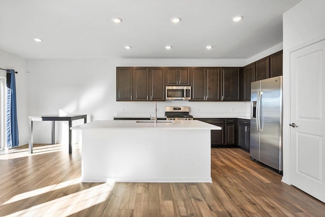 kitchen featuring dark wood-type flooring, appliances with stainless steel finishes, a kitchen island with sink, and dark brown cabinets