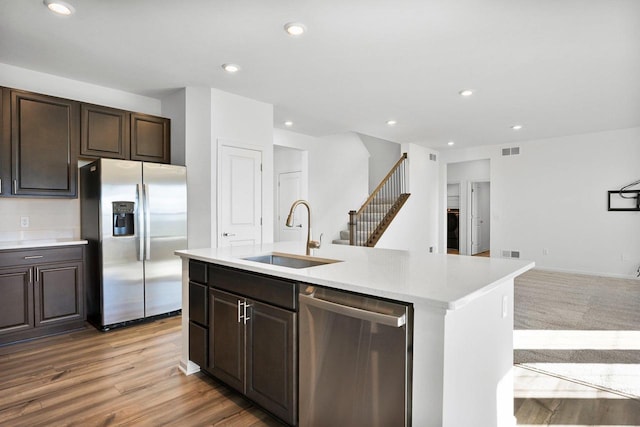 kitchen featuring dark brown cabinetry, sink, light hardwood / wood-style flooring, appliances with stainless steel finishes, and a kitchen island with sink