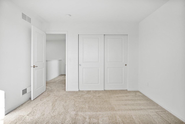 unfurnished bedroom with light colored carpet and a closet