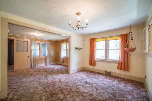 carpeted empty room with ornamental molding, wooden walls, and an inviting chandelier