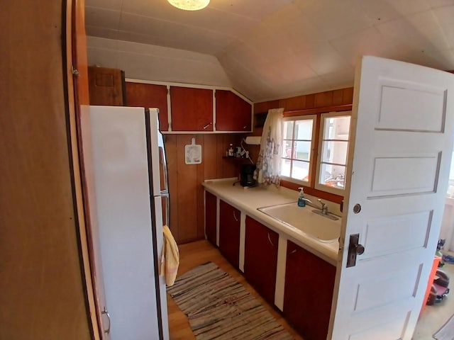 kitchen featuring white fridge, lofted ceiling, sink, and wooden walls