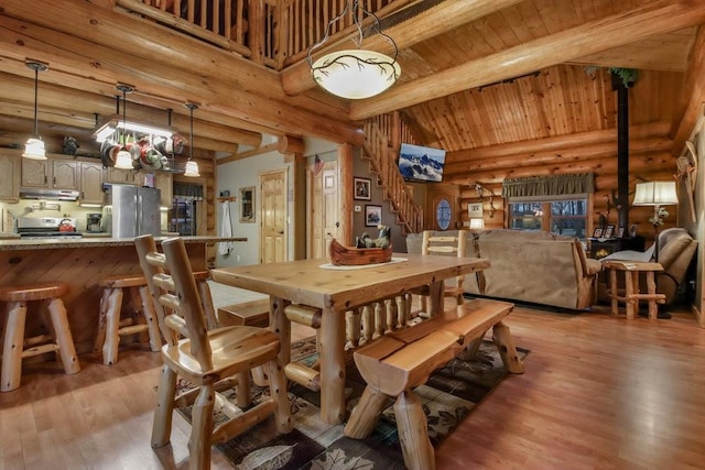 dining room featuring beamed ceiling, high vaulted ceiling, light hardwood / wood-style flooring, and rustic walls