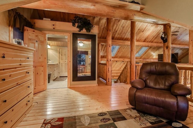 living area with beam ceiling, light hardwood / wood-style floors, a skylight, and wooden walls