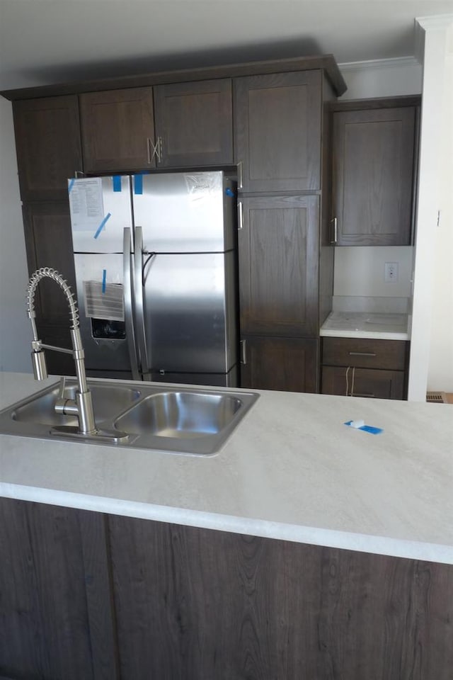 kitchen featuring stainless steel fridge, dark brown cabinetry, ornamental molding, and sink