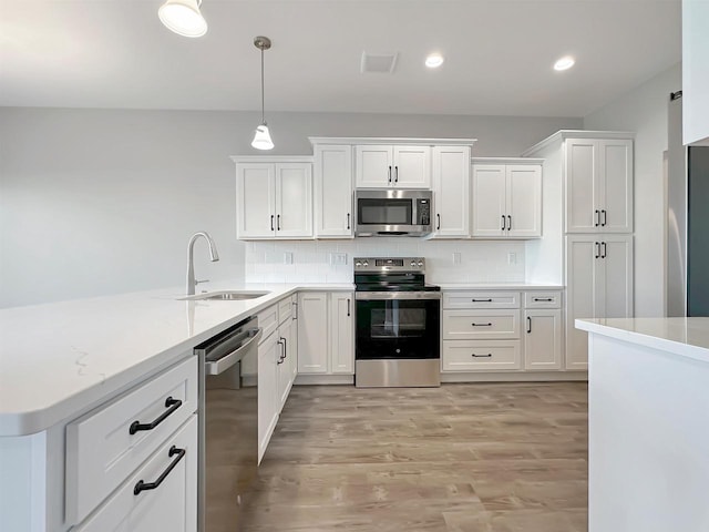 kitchen featuring white cabinetry, sink, hanging light fixtures, stainless steel appliances, and light hardwood / wood-style floors