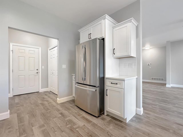 kitchen with tasteful backsplash, white cabinetry, stainless steel refrigerator, and light hardwood / wood-style flooring