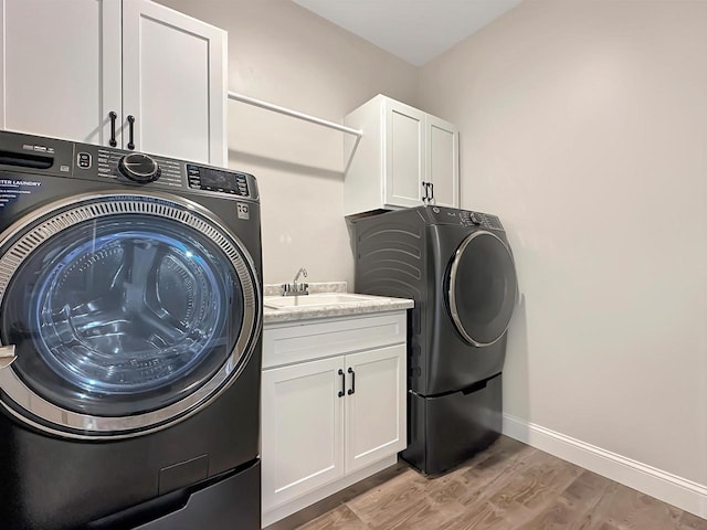 clothes washing area featuring independent washer and dryer, sink, cabinets, and light wood-type flooring