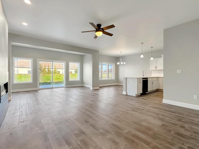 unfurnished living room featuring ceiling fan with notable chandelier, a large fireplace, light wood-type flooring, and sink