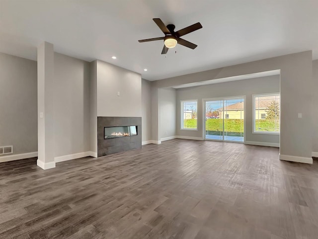 unfurnished living room with a tile fireplace, ceiling fan, and dark wood-type flooring