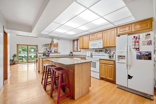 kitchen with a center island, a kitchen breakfast bar, kitchen peninsula, light hardwood / wood-style floors, and white appliances