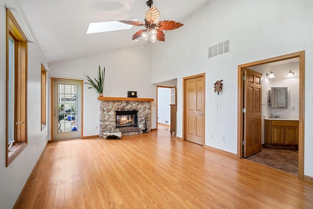 unfurnished living room featuring a skylight, ceiling fan, high vaulted ceiling, light hardwood / wood-style floors, and a fireplace