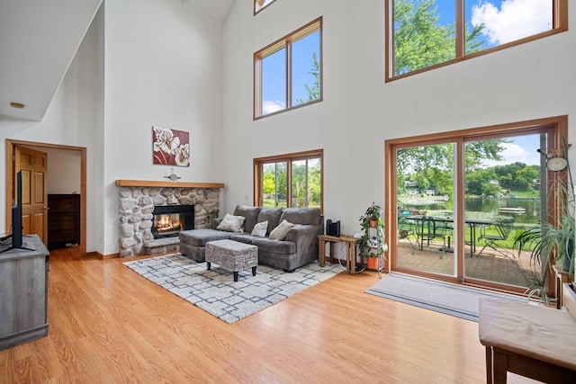 living room featuring a healthy amount of sunlight, a stone fireplace, light hardwood / wood-style floors, and a high ceiling