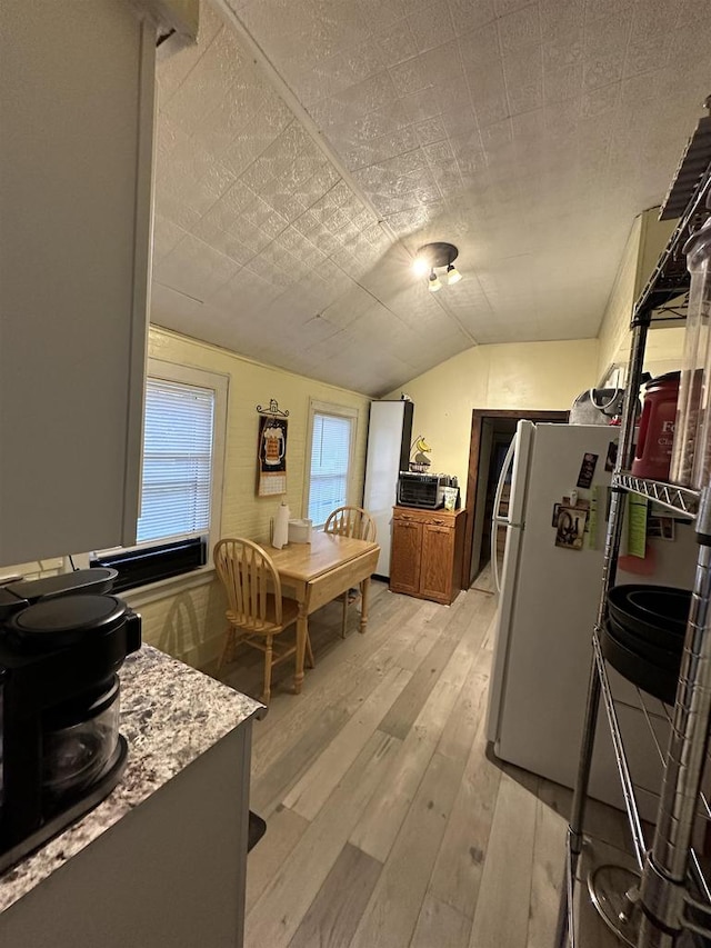 kitchen with white refrigerator, light stone countertops, light hardwood / wood-style flooring, and vaulted ceiling