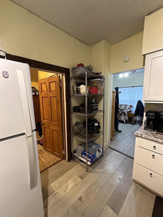 kitchen featuring white refrigerator, light stone countertops, white cabinetry, and light hardwood / wood-style flooring