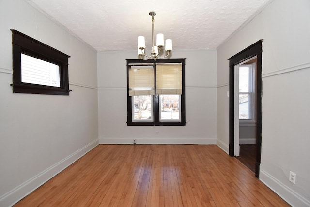 empty room featuring a textured ceiling, light wood-type flooring, and a chandelier