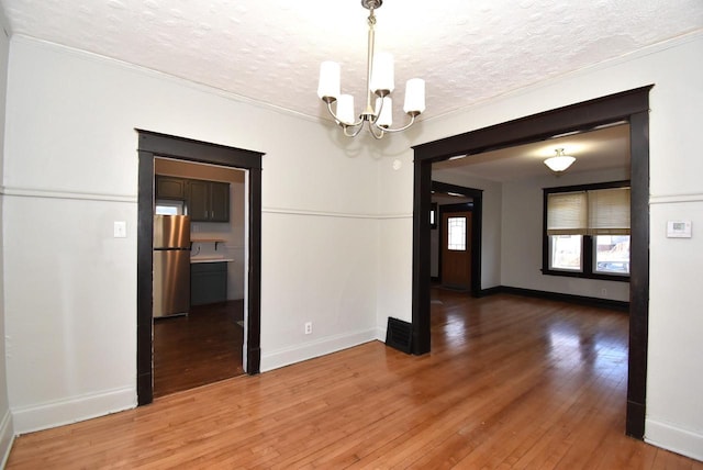 unfurnished dining area with hardwood / wood-style flooring, a textured ceiling, and a notable chandelier