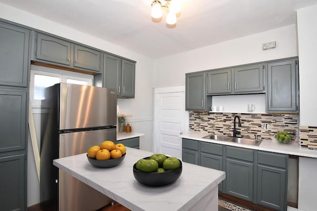 kitchen with stainless steel refrigerator, gray cabinets, tasteful backsplash, and sink