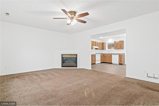 unfurnished living room featuring ceiling fan, sink, a textured ceiling, and light carpet