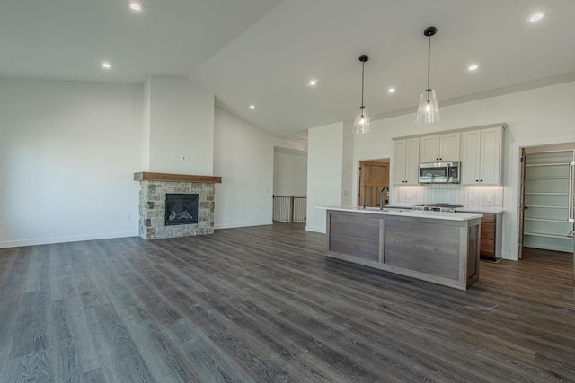 kitchen with dark hardwood / wood-style flooring, a kitchen island with sink, white cabinetry, hanging light fixtures, and a stone fireplace