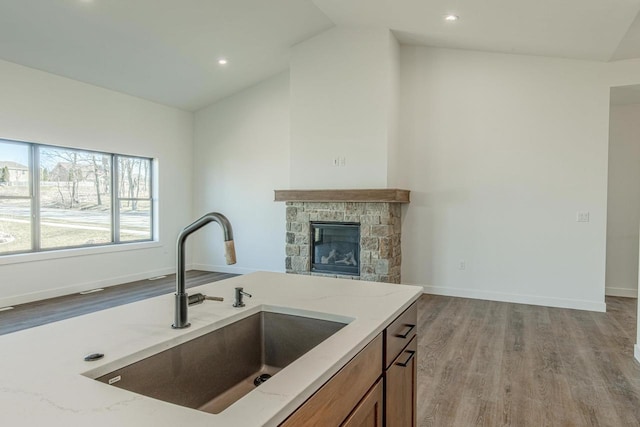 kitchen featuring light stone countertops, sink, a stone fireplace, light hardwood / wood-style floors, and vaulted ceiling