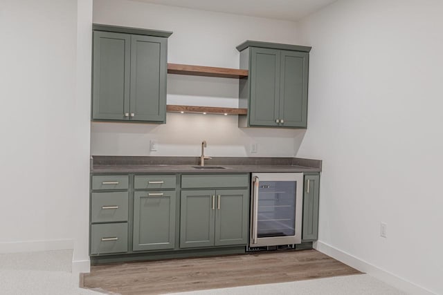 bar with green cabinets, sink, beverage cooler, and light wood-type flooring