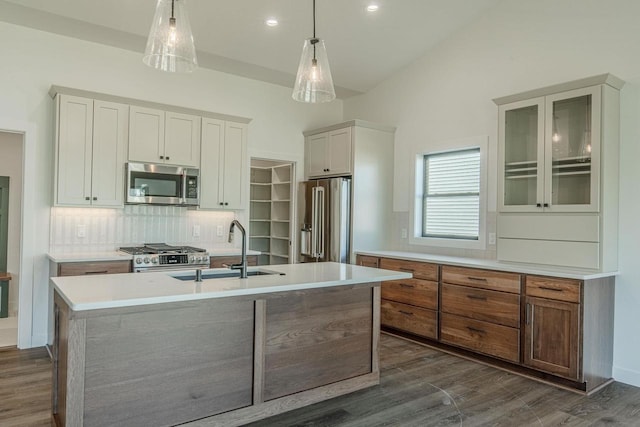 kitchen with sink, hanging light fixtures, stainless steel appliances, a kitchen island with sink, and white cabinets