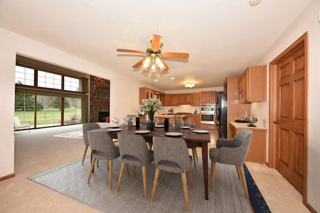 carpeted dining room featuring a stone fireplace and ceiling fan