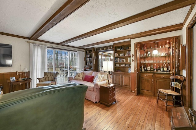 living room with beam ceiling, light wood-type flooring, a textured ceiling, and bar area