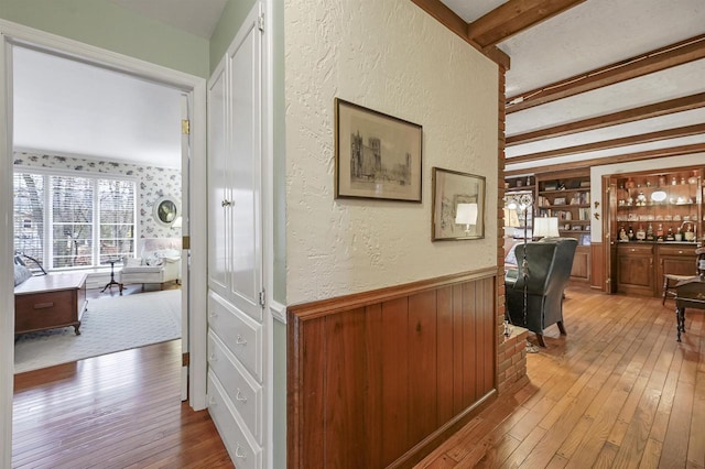 hallway featuring built in shelves, light hardwood / wood-style floors, and beam ceiling