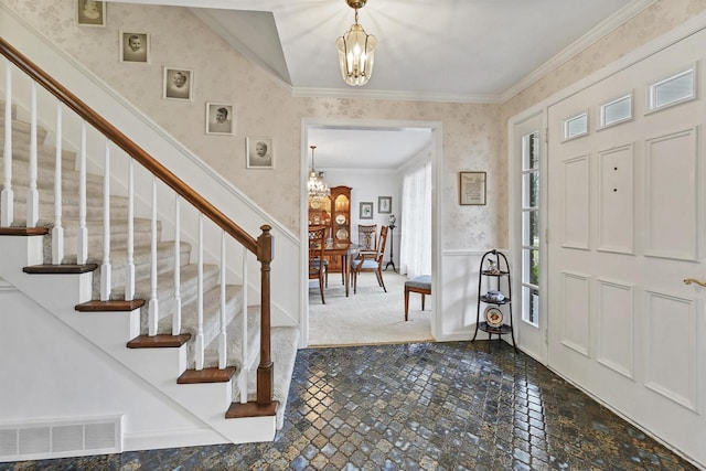 carpeted foyer entrance featuring ornamental molding and a notable chandelier