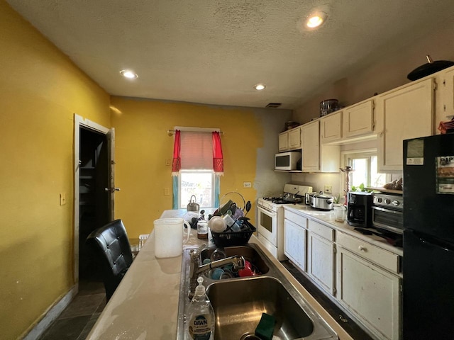 kitchen with black fridge, white gas stove, a healthy amount of sunlight, and a textured ceiling