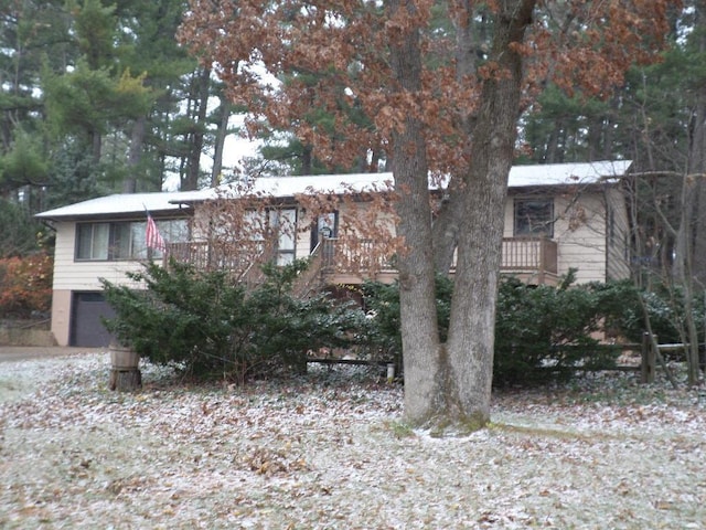 view of property hidden behind natural elements featuring a garage and a wooden deck