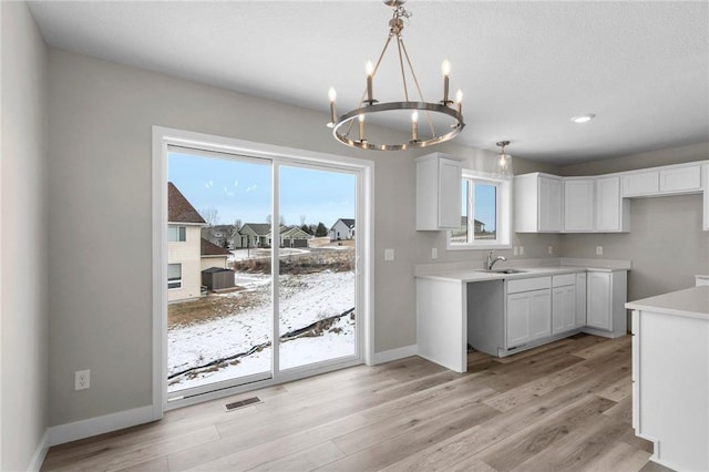 kitchen featuring sink, white cabinetry, a chandelier, light hardwood / wood-style flooring, and pendant lighting