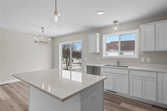 kitchen featuring sink, white cabinetry, light wood-type flooring, a kitchen island, and pendant lighting