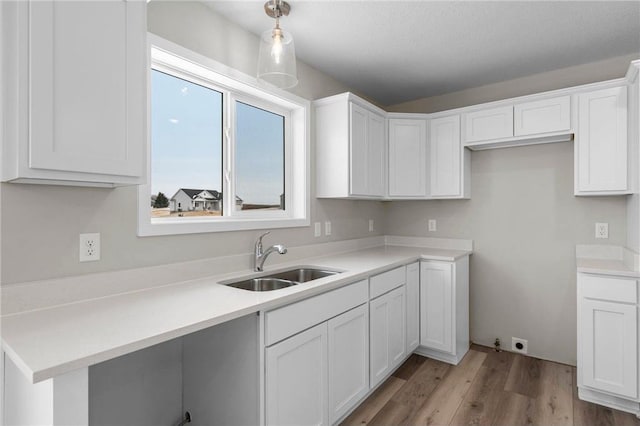 kitchen with sink, decorative light fixtures, light hardwood / wood-style floors, and white cabinets