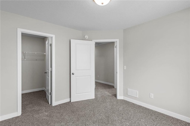 unfurnished bedroom with a spacious closet, carpet floors, a closet, and a textured ceiling