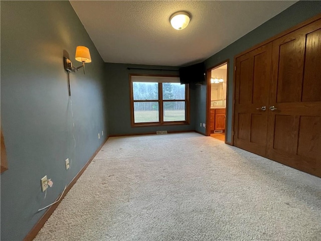 unfurnished bedroom with ensuite bath, light colored carpet, and a textured ceiling