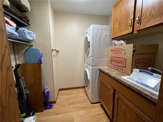 washroom with cabinets, stacked washer and clothes dryer, sink, light hardwood / wood-style flooring, and a textured ceiling