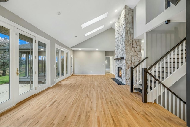 unfurnished living room with light hardwood / wood-style floors, a stone fireplace, high vaulted ceiling, and a skylight