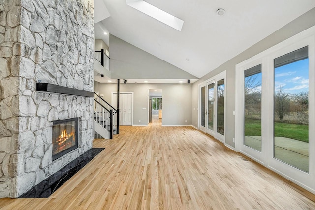 unfurnished living room with a fireplace, light hardwood / wood-style floors, high vaulted ceiling, and a skylight