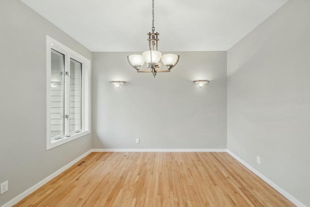 unfurnished room with a notable chandelier and light wood-type flooring