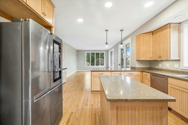 kitchen with light brown cabinets, stainless steel appliances, decorative light fixtures, and light hardwood / wood-style floors