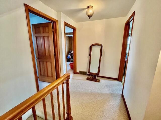 hallway featuring light carpet, visible vents, and baseboards