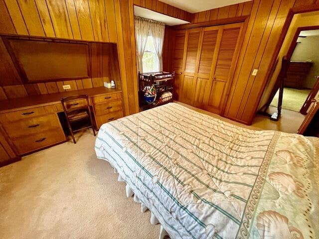 bedroom with a closet, light colored carpet, and wood walls